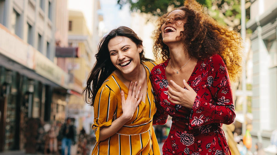 Two women laughing and walking outside in a city setting.